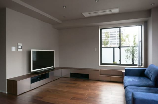 リビング／内装の床や壁の素材に合わせて、ブラックウォルナットと、ビーズブラスト加工を施したステンレスでテレビボードを設えた。上品な質感が高級感を醸すと共に、やわらかな反射光で空間の広がりを演出する