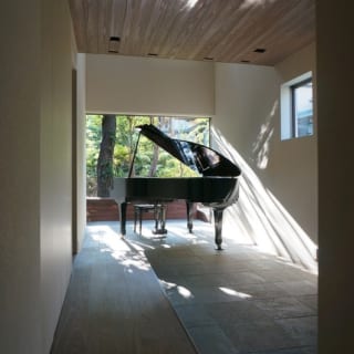 1階　土間にピアノ／空間がシンプルだからこそ屋外の緑がいきいきと輝き、ピアノそのものが美しいオブジェとして映える（※）
