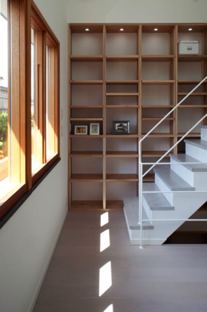 2階　書棚／ダイニングの一角には3階への階段がある。階段横の壁に造り付けた大きな書棚は自由な発想で使えるが、何も置かなくても絵になる。木製サッシと好相性の御影石の窓台もインテリアのポイント