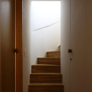 廊下から2階に上がる階段の様子。ほんのりと柔らかな光が差し込む。一見すると分からないが、壁の部分は収納スペースとなっている