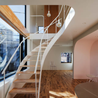 2階　ダイニング～リビング／階段の奥がリビング。ゆるやかなカーブを描く軽やかなデザインの階段は、景色を見ながら行き来する楽しさがある。階段まわりは吹抜けなので、2階と3階の一体感も高い。これだけ大きな窓があっても、1)適度な目隠しになる階段を窓際に配置　2）2階は窓を床まで開けず腰壁を設置　3)ダイニングをフロア奥に配置　という3つの工夫で、開放感を得ながらプライバシーも確保している