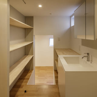 1階の洗面室。収納棚が豊富に設けられ、使い勝手が良い。数段下がった奥の部屋は主寝室