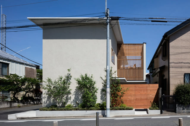 敷地は、東西北が道路に面する角地。建物の背面にあたる南側は隣家が迫り採光を望みにくい。そこで、敷地の南側に広いデッキを設け、デッキに入る光が家中に行きわたるプランで採光を確保。その分、道路面は壁が多くなったが、植栽によっていきいきとした表情を加えている