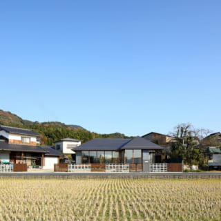 南側から見る全景。田んぼと北側の宮地岳による彩りが、四季の移ろいを感じさせる。道路境界は風通しのよい花ブロックと縦格子で、通行人からの視界を遮る