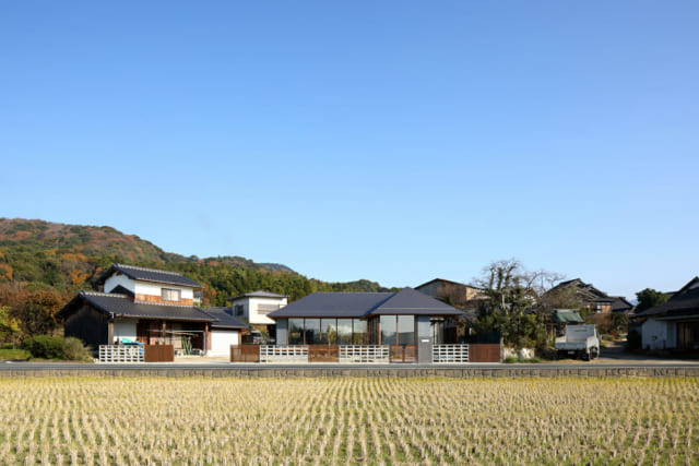 南側から見る全景。田んぼと北側の宮地岳による彩りが、四季の移ろいを感じさせる。道路境界は風通しのよい花ブロックと縦格子で、通行人からの視界を遮る