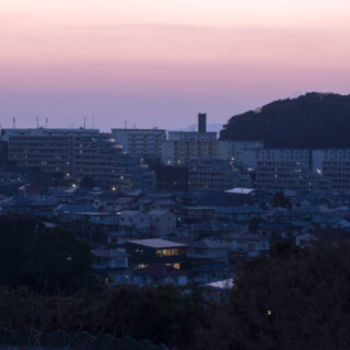 J邸が立つ住宅街を北から見た夕景。明かりがともる時間帯になると、北に大きな窓がない家が多い中、北向きに大開口を設けたJ邸がひときわ目立つ