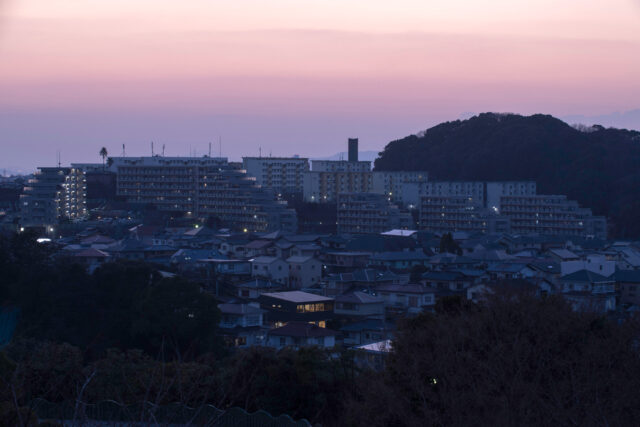 J邸が立つ住宅街を北から見た夕景。明かりがともる時間帯になると、北に大きな窓がない家が多い中、北向きに大開口を設けたJ邸がひときわ目立つ