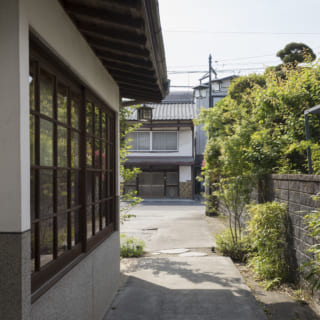 道路から玄関へのアプローチ。写真奥が道路で、右側に息子さん夫妻の住まいがある。左の窓は施主さまの寝室の窓。改修前の古い木枠を再利用して風情を残しつつ、内窓をつけて断熱性能を高めた