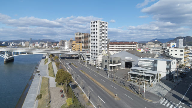 写真右手前、海沿いにあるカフェは街並みに馴染みつつも存在感を放つ。角地にあり道路と2面で接しているため、あえてどこからでも敷地に入れるような雰囲気をつくった。海側の植栽は店内から外を眺める人だけでなく、道行く人の目も楽しませている