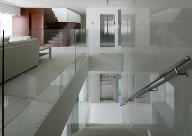 2階から1階への階段（手前）と3階への階段（奥）を一望するこの場所は、上質なモダン建築のお手本のようなスポット。手すり壁の強化ガラスは、支えの部材が見えない高度な設計。余計なものをそぎ落とした透明感あふれる空間が、階段や床の造形美を際立たせている
