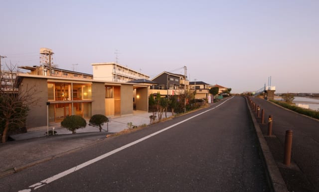 多摩川沿いの堤防道路から2mほど下がった敷地に立つS邸。どっしりと地面に根付く平屋づくりの外観が、おおらかな自然風景に馴染んでいる。シンプルなアウトラインとレイヤー状の壁がモダンな建築美を生み、人目を引く