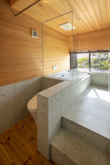 2階浴室。壁面は木材、床面は石材とナチュラルな素材を組み合わせリラックスできる空間に。窓は道路に面しているため、下から浴室内が見えないよう、窓枠の下ラインに合わせて縁側のようにフラットな面を設けた。天気がいい日は浴室から富士山も楽しめる