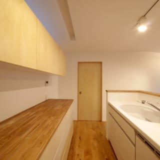 1階キッチン。キッチンは人造大理石カウンターのシステムキッチン。背後のカップボードや収納は造作し、LDK全体のインテリアと調和させている。写真奥の扉を開けると洗面室と浴室。家事をおこなう場所が1カ所にまとめられ、家事効率がアップ