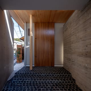 玄関前は道路側（写真左）をコンクリート壁で覆い、プライバシーを確保。中庭側（写真右）のコンクリート壁は型枠に杉板を使用することにより現れる柔らかな木目が自然のニュアンスとともに高級感を演出