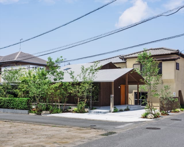 南東から見た外観。浦志の家が立つのは往来が多い東の道路（写真右）と南の生活道路（写真左手前）に面した南東角地。以前はご実家の別棟があった場所だ。長く低い軒が道路側をゆったり覆い、ずっと前からここに立っていたかのような控えめな印象となっている