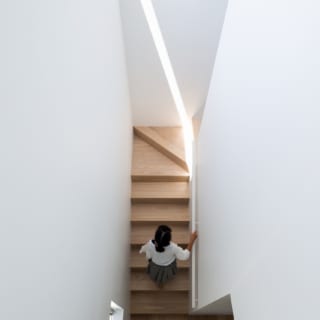 ハイサイド窓から明るい自然光が差し込む階段。真っ白な壁に光のラインが映える