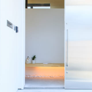 ステンレスで表面を覆った木製の引戸が特徴の玄関ポーチ。引戸を開けると腰を下ろせる腰掛ベンチがあり、下に間接正面としてライトを設置。その下に白い玉石を配置し、光を反射させている