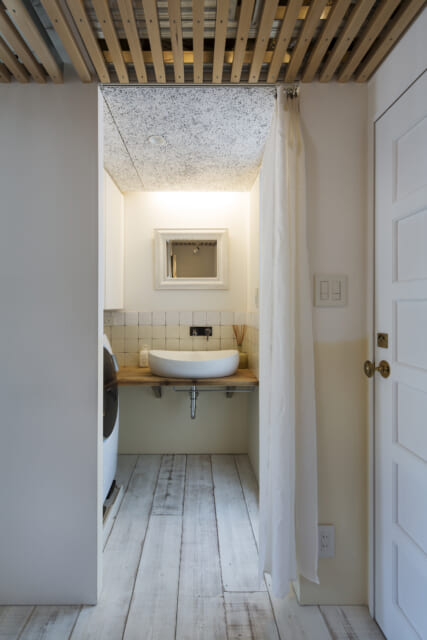 洗面脱衣室はカーテンですっきり仕切る。画像右のトイレの扉は、以前使われていたものに手を加え再利用した