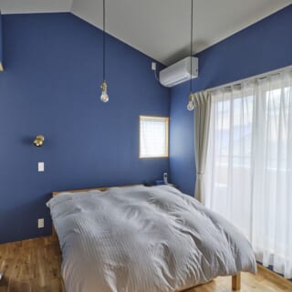 2階主寝室。壁は落ち着いたブルーで塗装。寝る前に読書するご夫妻のために、壁には真鍮の手元灯を設置