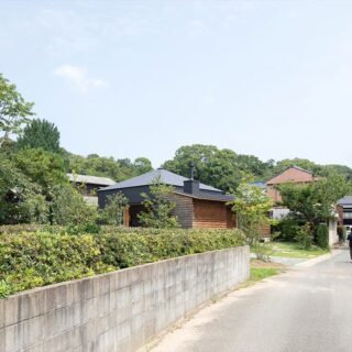 道路から見た「島の家001」。LDKとロフトのある方形屋根の部分を、高さを低く抑えた軒と焼杉の外壁の部分が囲み、集落の景観に溶け込んでいる。垣根がなくオープンな雰囲気ながら道路や隣家から距離を取って家を配置し、外から家の中の様子が直接見えてしまう心配をなくした