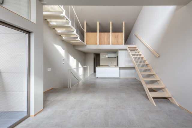 ２階LDK。キッチンの脇の通路は水回りに続く。キッチンの上部にはロフトを配置した。１階の雰囲気と合わせ、床にはコンクリートに似た柄のタイルを採用。収納はKさまがDIYするため空間はシンプルなデザインとし、床暖房など暮らしの快適性を高めるための設備を優先した