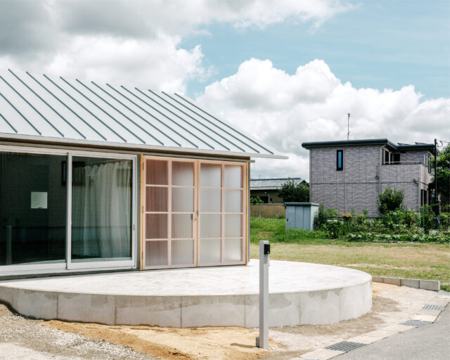 道路から家を見る。道路側のテラスは川の流れを思わせる円形で計画。円形は、どの方向からも人が集まって来やすいという利点もある。ポリカーボネート板の向こうはサンルーム。アルミサッシの部分にはダイニングがあり、サンルームと合わせて大きく開口できる