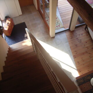 2階から玄関を見下ろす。床の素材は異なるが、ウッドデッキ（写真右奥）、玄関、LDK（右手前）は床がフラットにつながっている。庭から直接LDKに行くときも、玄関を通るときも、ウッドデッキを通過する造りで、ウッドデッキそのものがこの家の玄関のようでもある