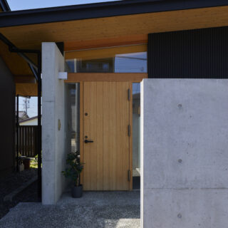 玄関のエントランス。玄関左のコンクリート壁は家の中へつながっている。屋根と黒い壁部はガルバリウム鋼板