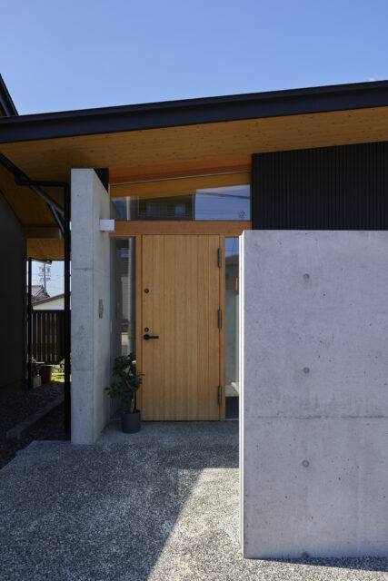 玄関のエントランス。玄関左のコンクリート壁は家の中へつながっている。屋根と黒い壁部はガルバリウム鋼板