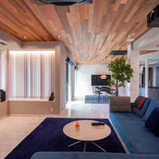 ブルーの家具が配置された開放的なリビング。床には⼤理⽯、天井にはレッドシダーを使⽤。
左⼿天井に仕込まれた電動スクリーンを下げるとホームシアターとなる
