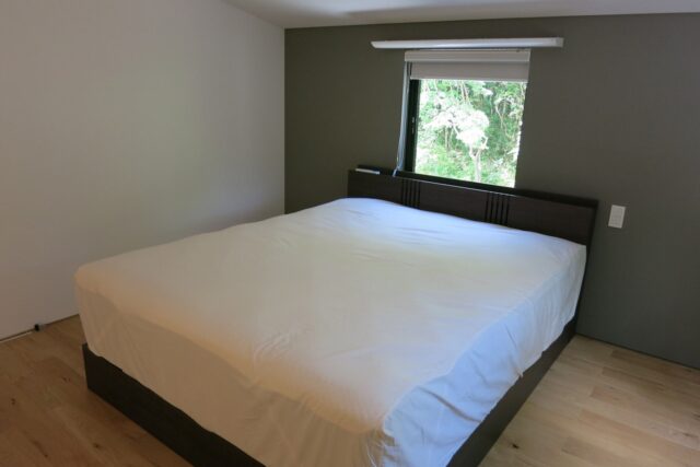 シンプルで落ち着きのある寝室。グリーンのアクセントウォールと窓先の緑のマッチングが心地よい