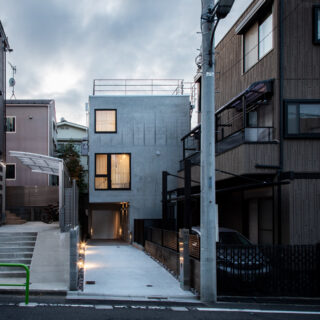 外観。画像中央奥が「武蔵関の住まい」。旗竿地のため道路まで距離があるという条件を生かし、道路に向かって大きく開口した。2階はLDKの窓。3階の窓は法的に必要な非常口でもある。大きさの違う正方形の窓をアクセントに、コンクリートの質感が引き立つデザインの外観とした