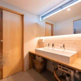 洗面所の正面はタイル張り。大きな鏡とシンクで１度に複数で使用が可能。隣のトイレへの扉はシナ合板と無垢板を合わせたもの。引手の形状も上田さんのこだわり。