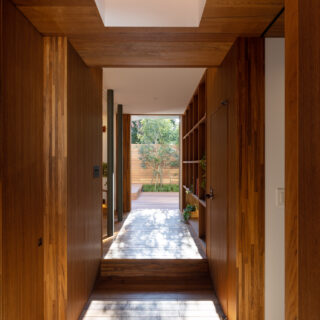 玄関からホールへとチーク材のトンネルが延びる。さらに視線の先には庭が見える。室内で高低差を解消するとともに「狭」から「広」に空間が変化することで、より開放感を感じさせる。