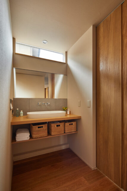 洗面コーナーは、上部に窓を設けワイドなミラーを採用することで、明るさと抜け感をもたらした。隣り合うトイレの扉も、天井までの高さのあるもので、高級感を演出。