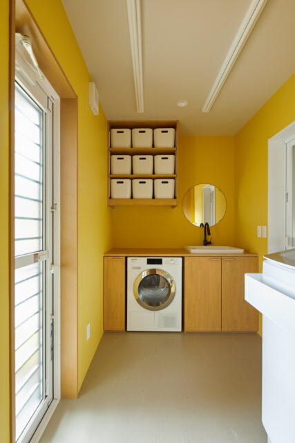 ランドリールームは、明るさをもたらす黄色の部屋に。天井には物干しのレールを設置。ミーレの乾燥機を入れられる高さに棚を造作。汚れものも洗える実験用シンクも設置し、家事に優しい設計。