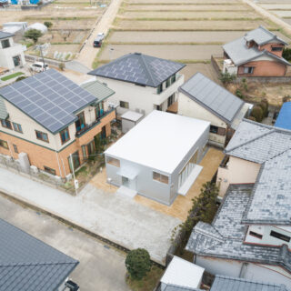 画像中央、白いフラットな屋根の建物が「幸田町の住宅」。旗竿地にあり、三方を隣家に囲まれている。隣家と距離を取って建物を配置することで、お互いに圧迫感なく暮らせる