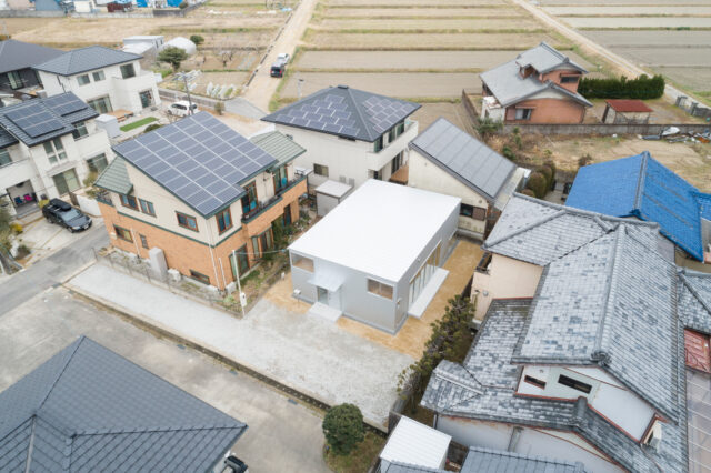 画像中央、白いフラットな屋根の建物が「幸田町の住宅」。旗竿地にあり、三方を隣家に囲まれている。隣家と距離を取って建物を配置することで、お互いに圧迫感なく暮らせる