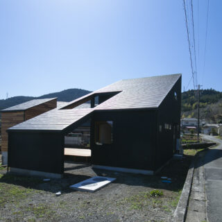 外観。大きな片流れ屋根の家の中から一部分がすっぽり抜け、小屋として少し離れたところにある。土地に段差があり、母屋は上の土地、小屋は下の土地に配置した。「段差があるからこそできた家にしたかった」と武本さん。２棟はウッドデッキで繋がり、行き来しやすい