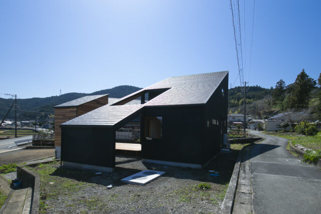 外観。大きな片流れ屋根の家の中から一部分がすっぽり抜け、小屋として少し離れたところにある。土地に段差があり、母屋は上の土地、小屋は下の土地に配置した。「段差があるからこそできた家にしたかった」と武本さん。２棟はウッドデッキで繋がり、行き来しやすい