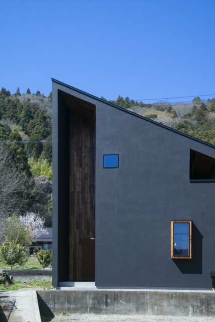 家は大胆な片流れ屋根のフォルムに、玄関部分の上まで貫かれた異なる素材の壁のラインと、目を引くデザイン