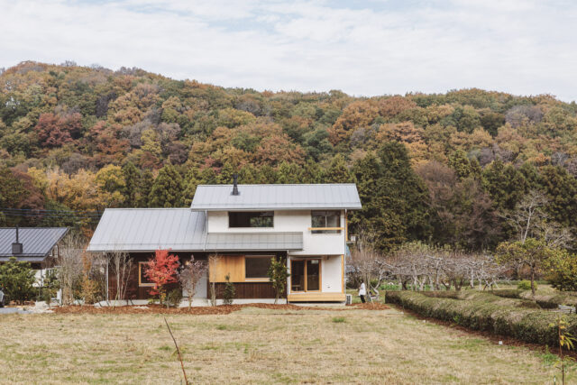 外観。画像左側にあたる西以外は、山（北）、原っぱ（南）、伸びやかに広がる眺望（東）とすこぶるいい環境の中にある「にちにちの家」。この環境に似合う木の家として、モダンすぎず、野暮ったくもないデザインを目指した。白、シルバーに木の風合いの茶をプラスした、軽やかな家