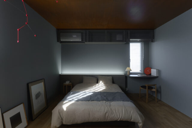 寝室。入眠効果を高めるため、暗めの配色で落ち着いた空間となっている。枕元には造作ボードを配し、こちらにも間接照明が組み込まれている
