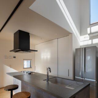 キッチンの一部は、北側の吹き抜けになっていて、こちらも２階の部屋と緩やかにつながる。背面の収納にモノを入れることで、生活感を出さない工夫も。