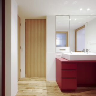 2階洗面室。建具や鏡を天井までのフルハイトで計画。コンパクトな空間であるが広さが感じられる。正面の扉は収納スペースへ、左奥の扉はトイレに続く。左手前は階段室