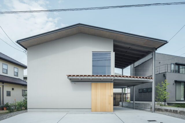 外観（正面）。周囲は住宅街で一般的な家であるため、奇抜な外観ではなく周囲に溶け込むシンプルなものとした。視線カットと断熱効果を高めるため、前面道路側の窓は最小限に。玄関ドアはバイクを土間に入れるため大きなものを造作した