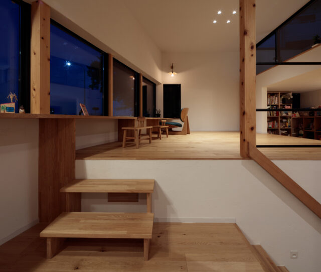 夜になると室内は落ち着きの空間に。窓側のランプは松田さんが手作りで仕上げたという。ＤＫとリビングの段差は、椅子の高さを計算した絶妙な高低差であるとともに、床下エアコンの風の通り道にもなっている。