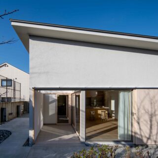庭の樹々に迎えられながら進んだ先にあるエントランス。大きな檜板張りの扉は、玄関扉や雨戸の役割も。吊り戸とすることでバリアフリーも。