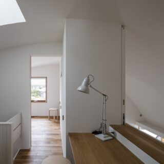 2階の吹き抜けに接する開口部には造作テーブルを配置。写真ではわかりずらいが、中央の造作家具から壁を引き出すことができる。来客時など、必要な時に空間を閉じられるアイデアだ。レールが見えて壁の開放時に曲面が分断されない工夫もされている