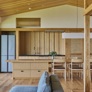 2階リビングエリアからダイニングキッチンを見る。自炊だけでなくケータリングにも対応できる広めのカウンターが使いやすい。食卓では誰もが均等に海を眺められるよう配置を工夫。雰囲気に合わせダイニングテーブル上部の照明は造作した。右の仕切り戸を入ると水回りへ続く